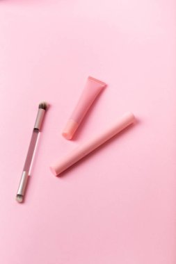 Pembe şişedeki maskara, pembe arka planda göz fırçası ve dudak parlatıcısı. Makyaj araçları