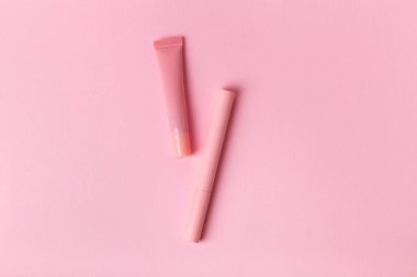 Mascara pembe şişede ve dudak parlatıcısı pembe arka planda. Makyaj araçları