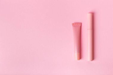 Mascara pembe şişede ve dudak parlatıcısı pembe arka planda. Makyaj araçları