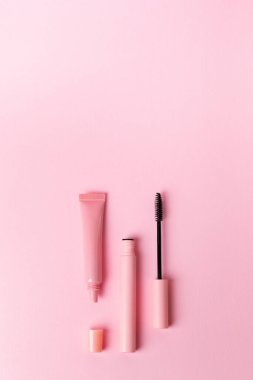 Mascara pembe şişede ve dudak parlatıcısı pembe arka planda. Makyaj araçları