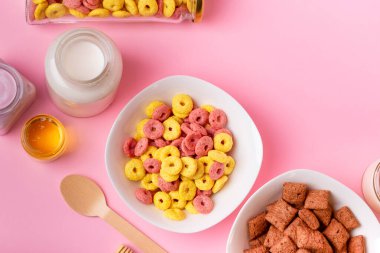 Kuru kahvaltı ve süt. Kuru tatlı kahvaltı - mısır halkaları, çikolatalı mısır yastıkları ve granola, süt, yoğurt ve bal pembe arka planda. Hızlı ve besleyici bir kahvaltı.