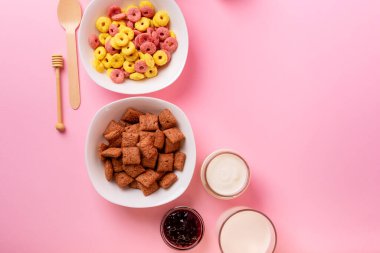 Kuru kahvaltı ve süt. Kuru tatlı kahvaltı - mısır halkaları, çikolatalı mısır yastıkları, süt, yoğurt ve pembe arka planda bal. Hızlı ve besleyici bir kahvaltı.