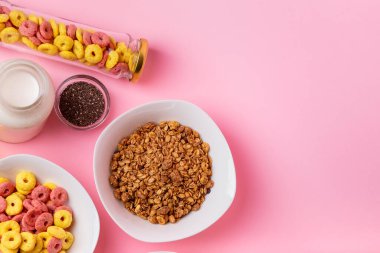 Kuru kahvaltı ve süt. Kuru tatlı kahvaltı - mısır halkaları, çikolatalı mısır yastıkları ve granola, süt, yoğurt ve bal pembe arka planda. Hızlı ve besleyici bir kahvaltı.