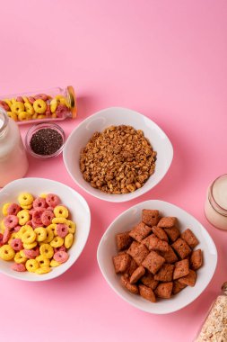 Kuru kahvaltı ve süt. Kuru tatlı kahvaltı - mısır halkaları, çikolatalı mısır yastıkları, süt, yoğurt ve pembe arka planda bal. Hızlı ve besleyici bir kahvaltı.