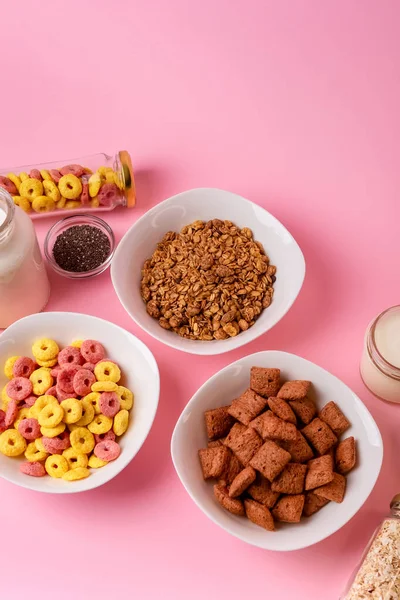 Kuru kahvaltı ve süt. Kuru tatlı kahvaltı - mısır halkaları, çikolatalı mısır yastıkları, süt, yoğurt ve pembe arka planda bal. Hızlı ve besleyici bir kahvaltı.