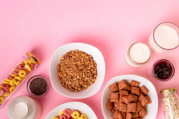 Kuru kahvaltı ve süt. Kuru tatlı kahvaltı - mısır halkaları, çikolatalı mısır yastıkları, süt, yoğurt ve pembe arka planda bal. Hızlı ve besleyici bir kahvaltı.