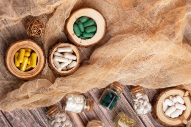 Küçük cam kavanozlarda çeşitli vitaminler, mineraller ve gıda takviyeleri ve ahşap arka planda ristik tarzda yukarıdan ahşap tabaklar. Bağışıklık sistemini geliştirmek için besin takviyesi hapları. Mutlu ve sağlıklı bir yaşam tarzı.