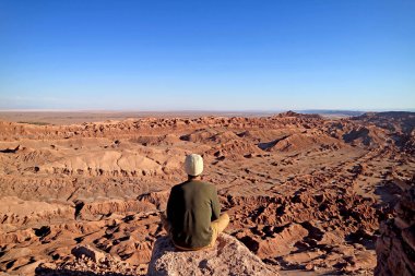 Rocky Kayalıklarında oturan yürüyüşçü Ay Vadisi 'nin inanılmaz manzarasını ya da Şili Çölü' ndeki Valle de la Luna 'yı hayranlıkla izliyor.