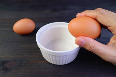 Bir adamın eli yumurta tutarken yemek pişirmek için bir kase kırar.