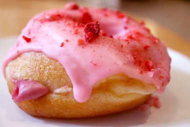 Closeup of mouthwatering strawberry-glazed with raspberry cream filling doughnut on a white plate
