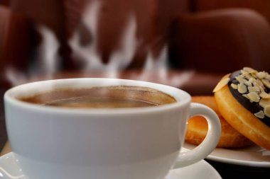 Yükselen Buharlı bir fincan sıcak kahve ve arka planda bir tabak çörek.