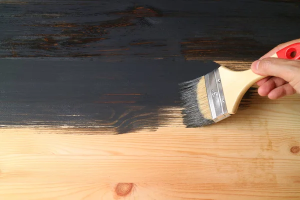Man's hand painting surface of natural wood plank into black color