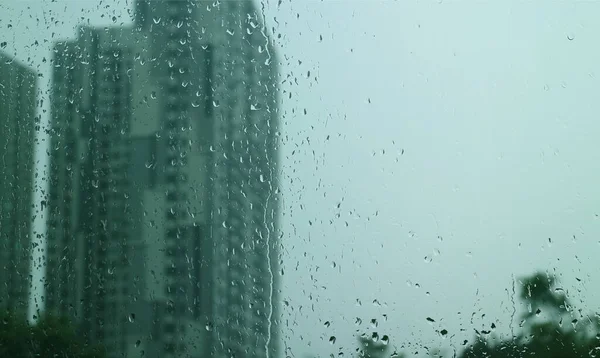 用模糊的摩天大楼和阴云密布的天空遮住窗玻璃上雨滴的纹理 — 图库照片