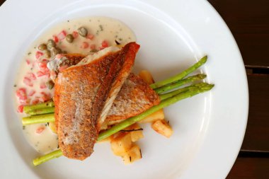 Tavada kurutulmuş levrek, beyaz tabakta domates kapari, hardal krema sosu.