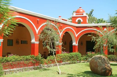 Güney Amerika 'nın Peru bölgesindeki Huacachina kasabasında çiçek açan bahçeli canlı kırmızı renkli bir bina.