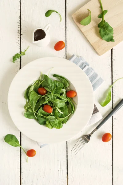 Rocket salad dengan tomat ceri pada latar belakang kayu putih — Stok Foto