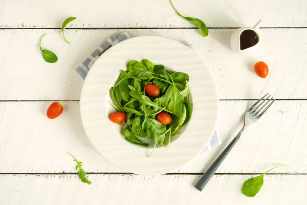 Rocket salad dengan tomat ceri pada latar belakang kayu putih — Stok Foto