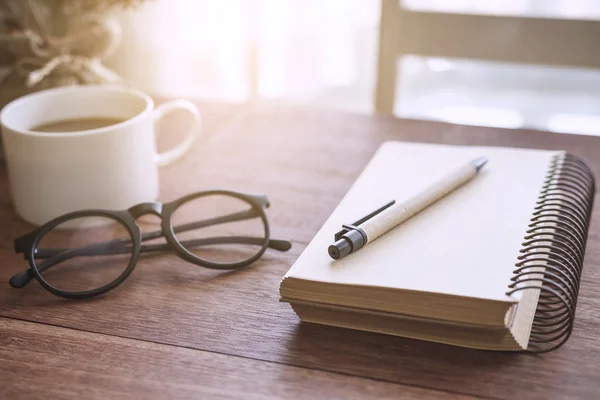 Cuaderno y taza de café con luz solar en la oficina del escritorio — Foto de Stock