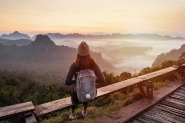 Genç kadın gezgin dağın üzerinden sis ve gün batımına bakıyor.