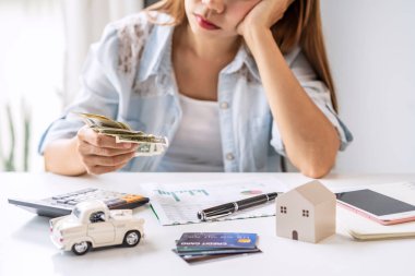 Stresli genç kadın aylık ev giderlerini, vergileri, banka hesaplarını ve kredi kartı ekstrelerini hesaplıyor.