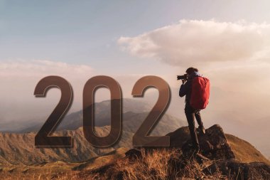 Sırt çantalı genç bir gezgin dağda fotoğraf çekiyor. 2021 Macera Yolculuğu yaşam tarzı konsepti.