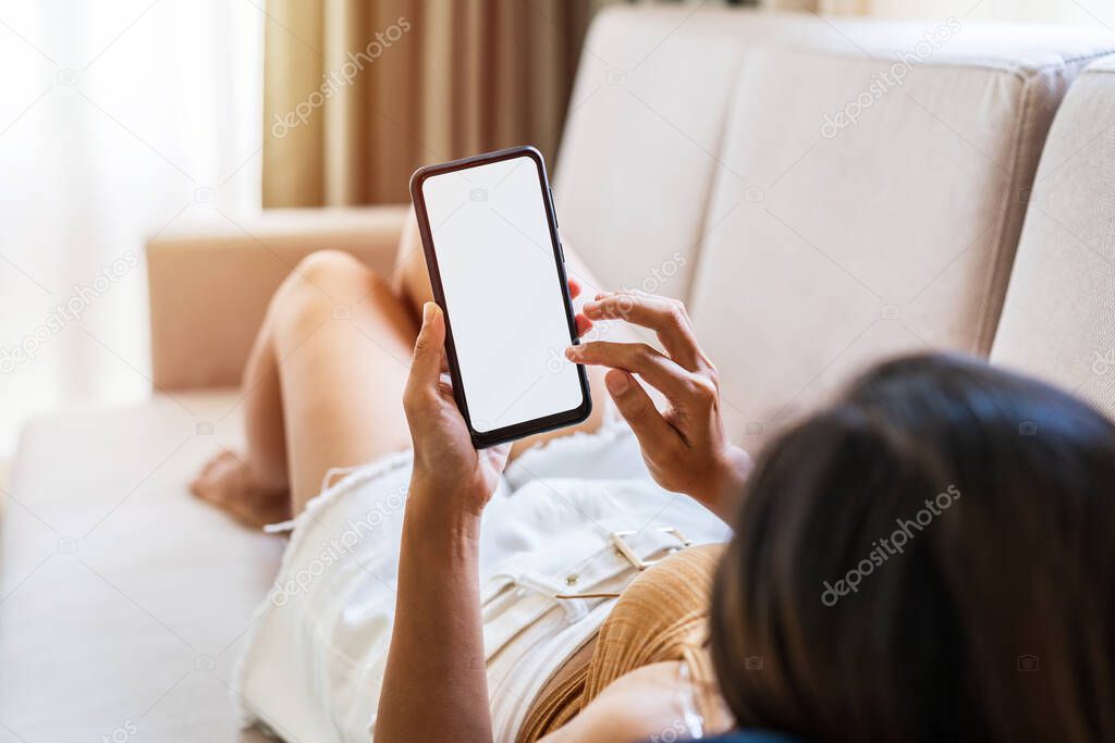 Young woman lying on sofa at living room and using smart phone at home
