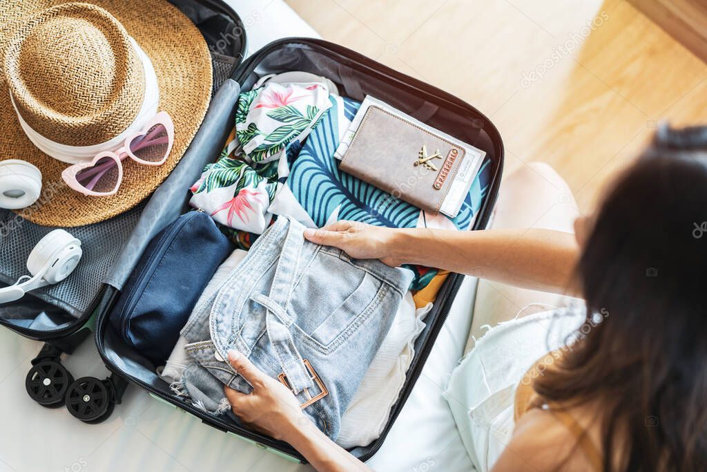 Young woman traveler sitting on the bed packing her suitcase preparing for travel on summer vacation