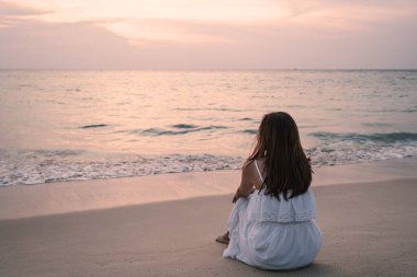 Yalnız genç Asyalı kadın gün batımında sahilde oturuyor.