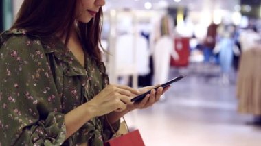 Alışveriş çantalı genç Asyalı kadın akıllı telefon kullanıyor ve alışveriş merkezinde alışveriş yapıyor, kadın yaşam tarzı konsepti.