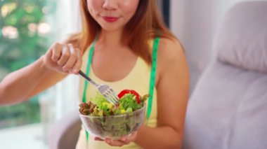 Evde ev yapımı sağlıklı salata yiyen genç bir kadın sağlıklı beslenme tarzı ve diyet konsepti.