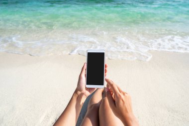 Güzel tropikal beyaz kumsalda cep telefonu kullanan genç bir kadın. Dalgalı ve şeffaf deniz, yaz tatili ve fotokopi alanı olan seyahat kavramı.