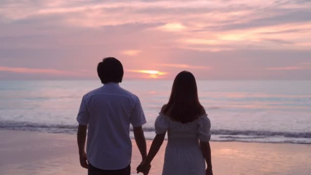 若いアジアのカップルが手を携えて一緒にビーチで美しい夕日を見て 夏休みのコンセプト — ストック動画