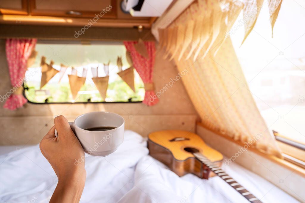 Young woman traveler with cup of coffee laying in camper van and looking beautiful landscape while road trip traveling on vacation
