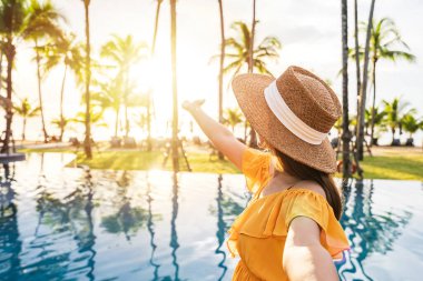 Genç bayan gezgin yaz tatili için seyahat ederken tropik bir tatil havuzu kenarında gün batımının tadını çıkarıyor.