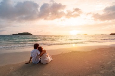 Genç Asyalı çift sakin plajda gün batımını seyrediyor, yaz tatili konsepti.