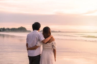 Genç Asyalı çift sahilde gün batımını seyrediyor, yaz tatili konsepti.