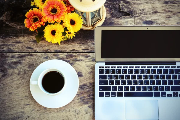 a cup of coffee and laptop on wood floor with flower