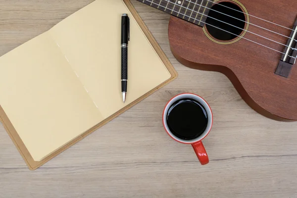 Tasse Kaffee mit Ukulele und Notizbuch auf Holztisch — Stockfoto