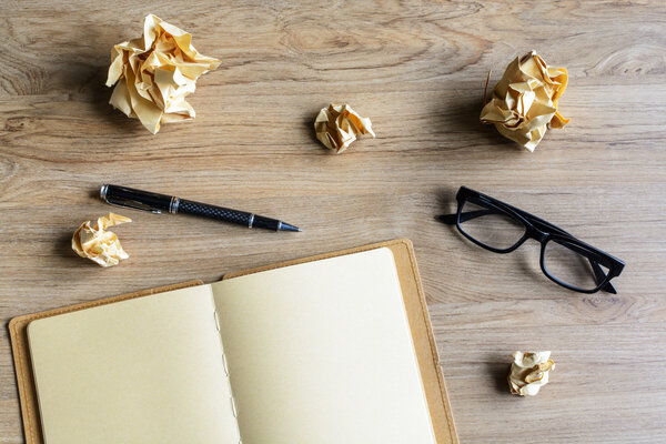 Crumpled paper balls with eye glasses and notebook on wood desk