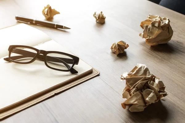 Bolas de papel arrugadas con anteojos y cuaderno sobre escritorio de madera — Foto de Stock