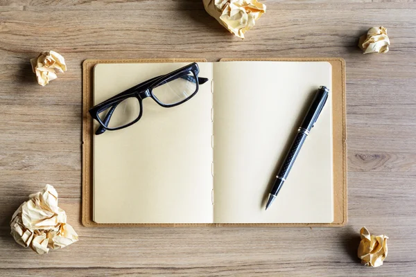 Bolas de papel arrugadas con anteojos y cuaderno sobre escritorio de madera — Foto de Stock