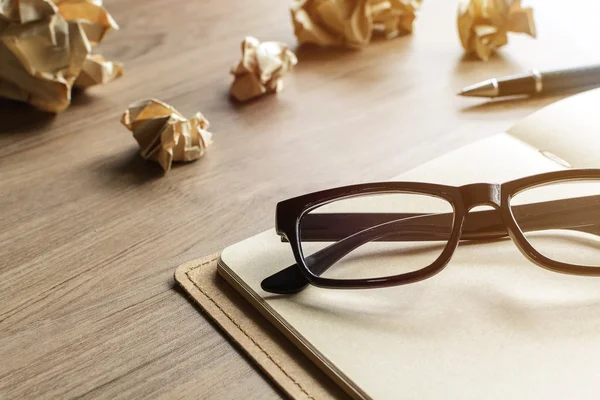 Bolas de papel arrugadas con anteojos y cuaderno sobre escritorio de madera — Foto de Stock