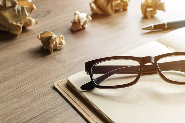 Crumpled paper balls with eye glasses and notebook on wood desk