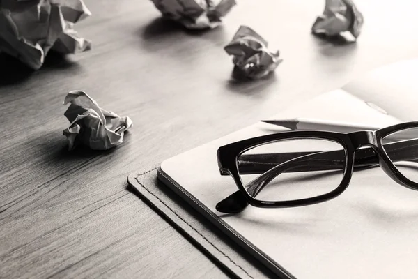 Смятые бумажные шарики с очками и блокнотом на деревянном столе — стоковое фото