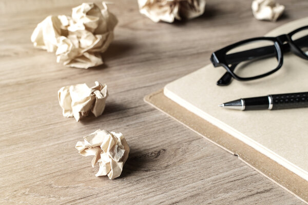 Crumpled paper balls with eye glasses and notebook on wooden des