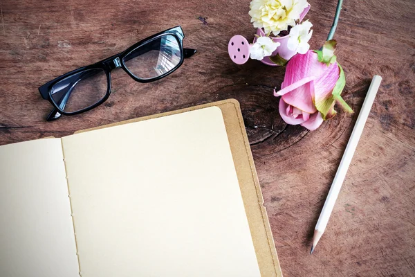 Cuaderno abierto en blanco con flores y vasos sobre mesa de madera — Foto de Stock