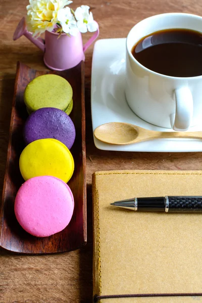 Macarrones coloridos y una taza de café con cuaderno — Foto de Stock