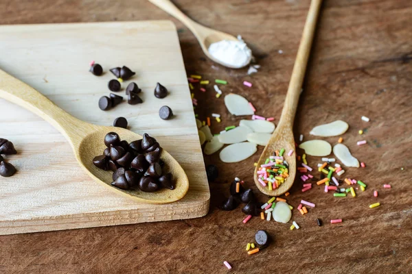 Chocolate chips on wooden spoon and ingredients — Stock Photo, Image