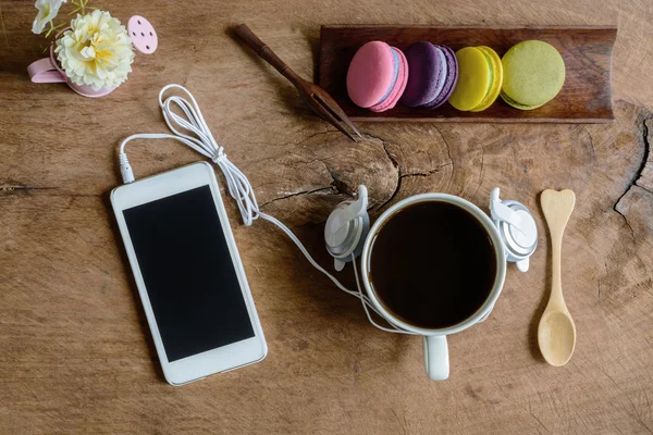 Macarrones coloridos y una taza de café con teléfono celular en madera — Foto de Stock