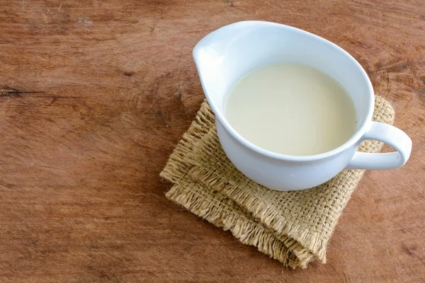 Milchkrug mit Sacktuch auf altem Holztisch — Stockfoto